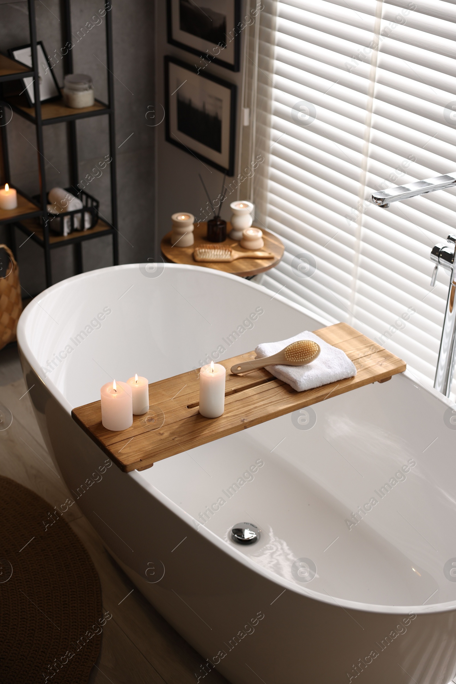 Photo of Wooden tray with burning candles, towel and brush on bathtub in bathroom