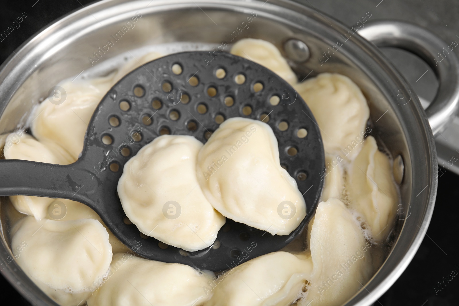 Photo of Boiling delicious dumplings (varenyky) on skimmer over pot, closeup