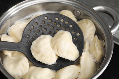 Photo of Boiling delicious dumplings (varenyky) on skimmer over pot, closeup