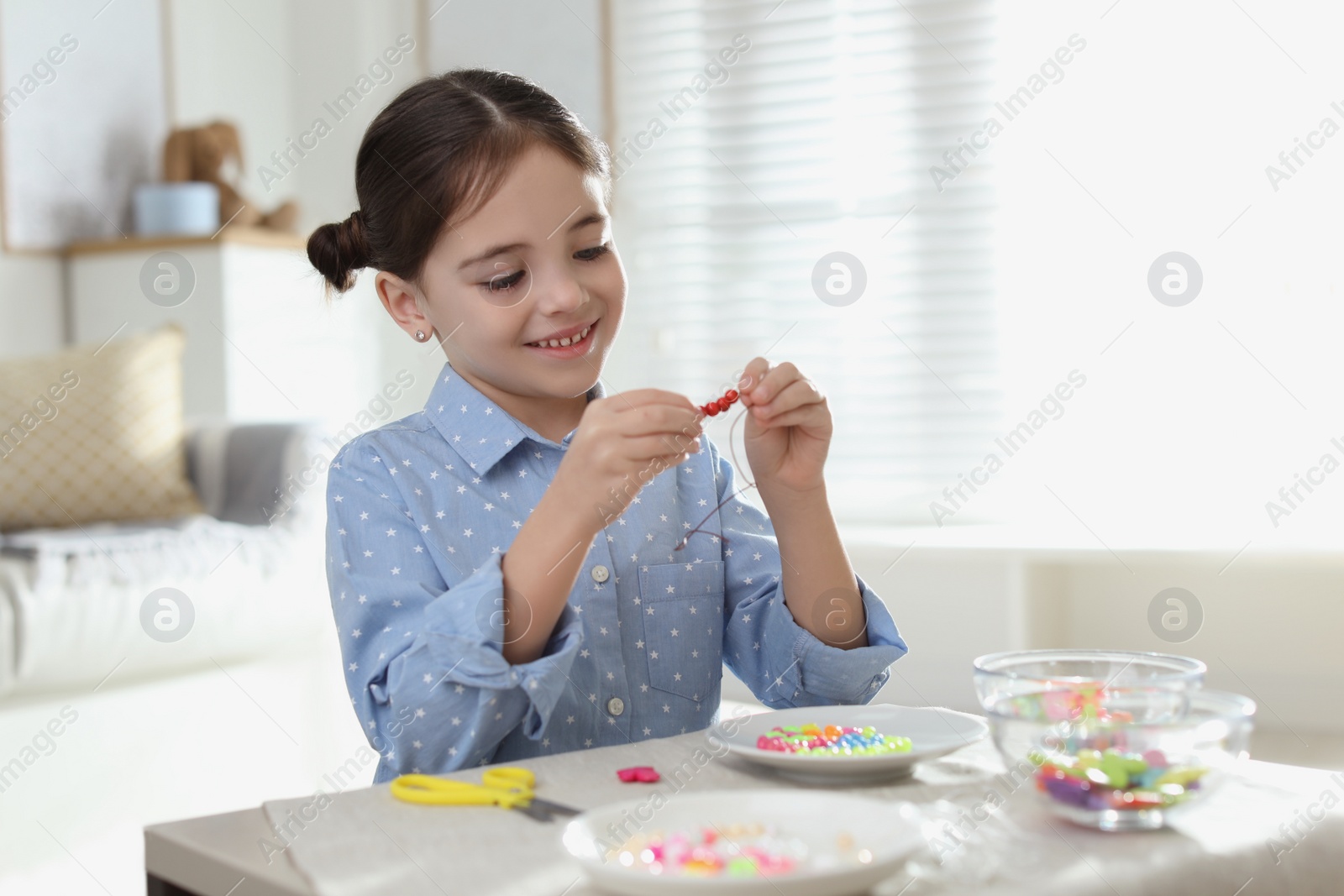 Photo of Little girl making accessory with beads at table indoors. Creative hobby