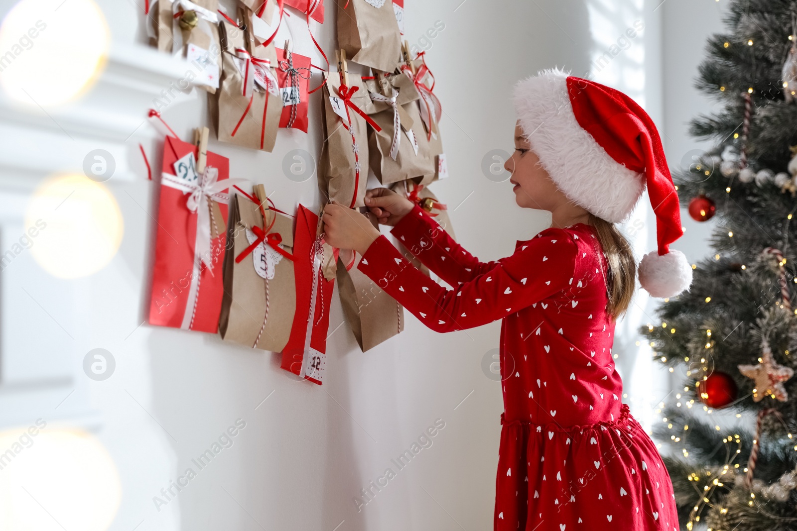 Photo of Cute little girl in Santa hat taking gift from Christmas advent calendar at home