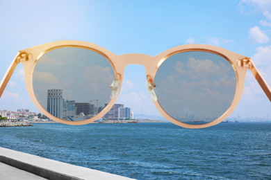 Image of Modern buildings near sea on sunny day, view through sunglasses