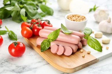 Photo of Fresh raw vegetarian sausages with basil, soybeans and vegetables on white marble table
