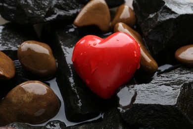 Red decorative heart on stones and water, closeup