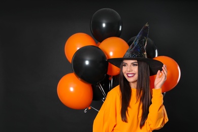 Beautiful woman wearing witch costume with balloons for Halloween party on black background