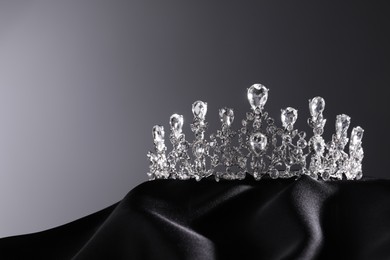 Photo of Beautiful silver tiara with diamonds on dark cloth against grey background. Space for text