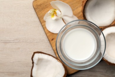 Glass of delicious vegan milk, coconuts and flower on white wooden table, flat lay. Space for text