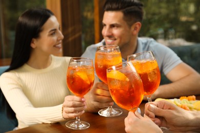 Friends clinking glasses of Aperol spritz cocktails at table, focus on hands
