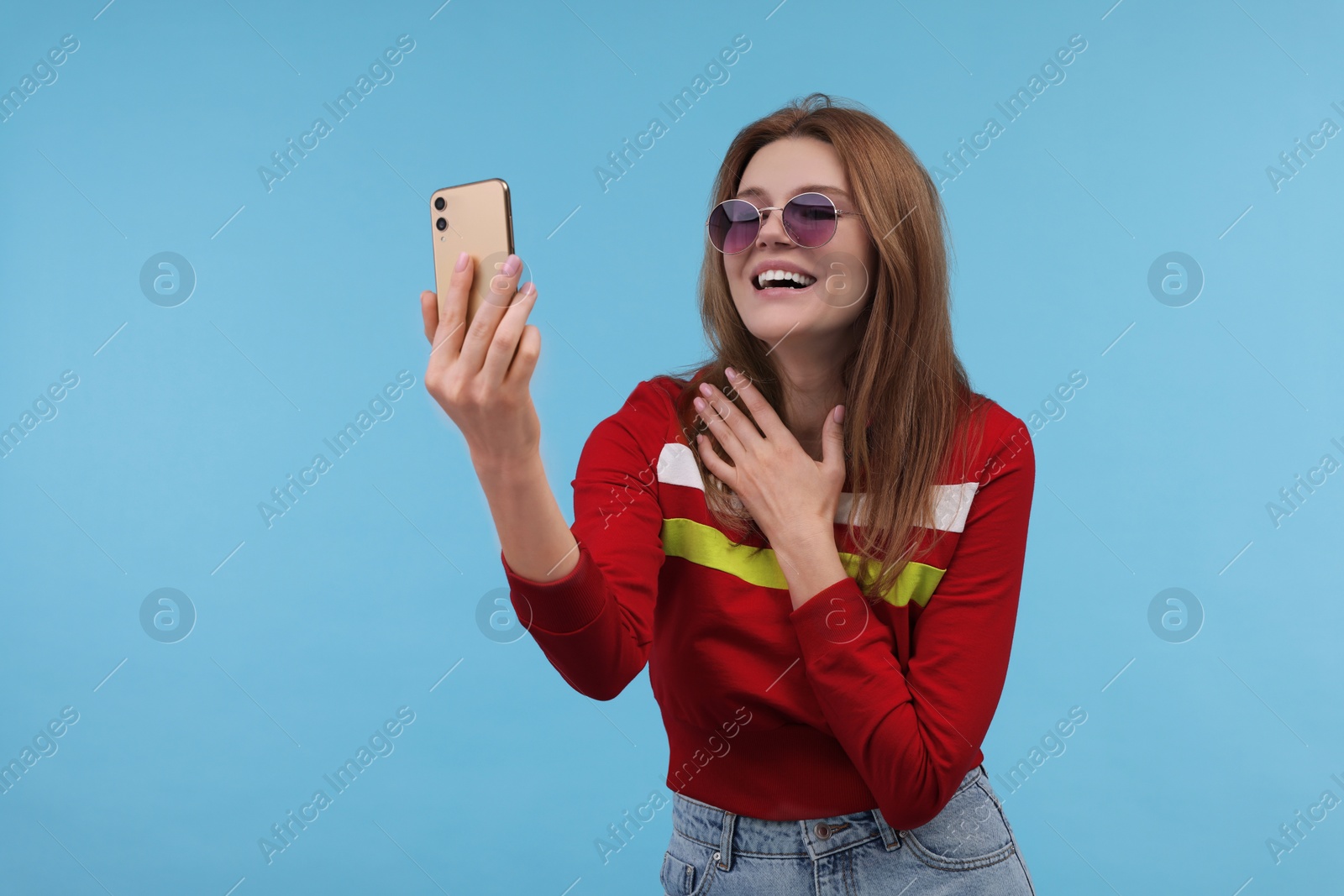 Photo of Beautiful woman in sunglasses taking selfie on light blue background