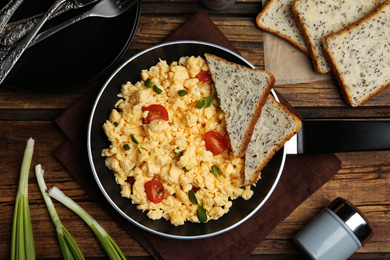 Photo of Tasty scrambled eggs served on wooden table, flat lay