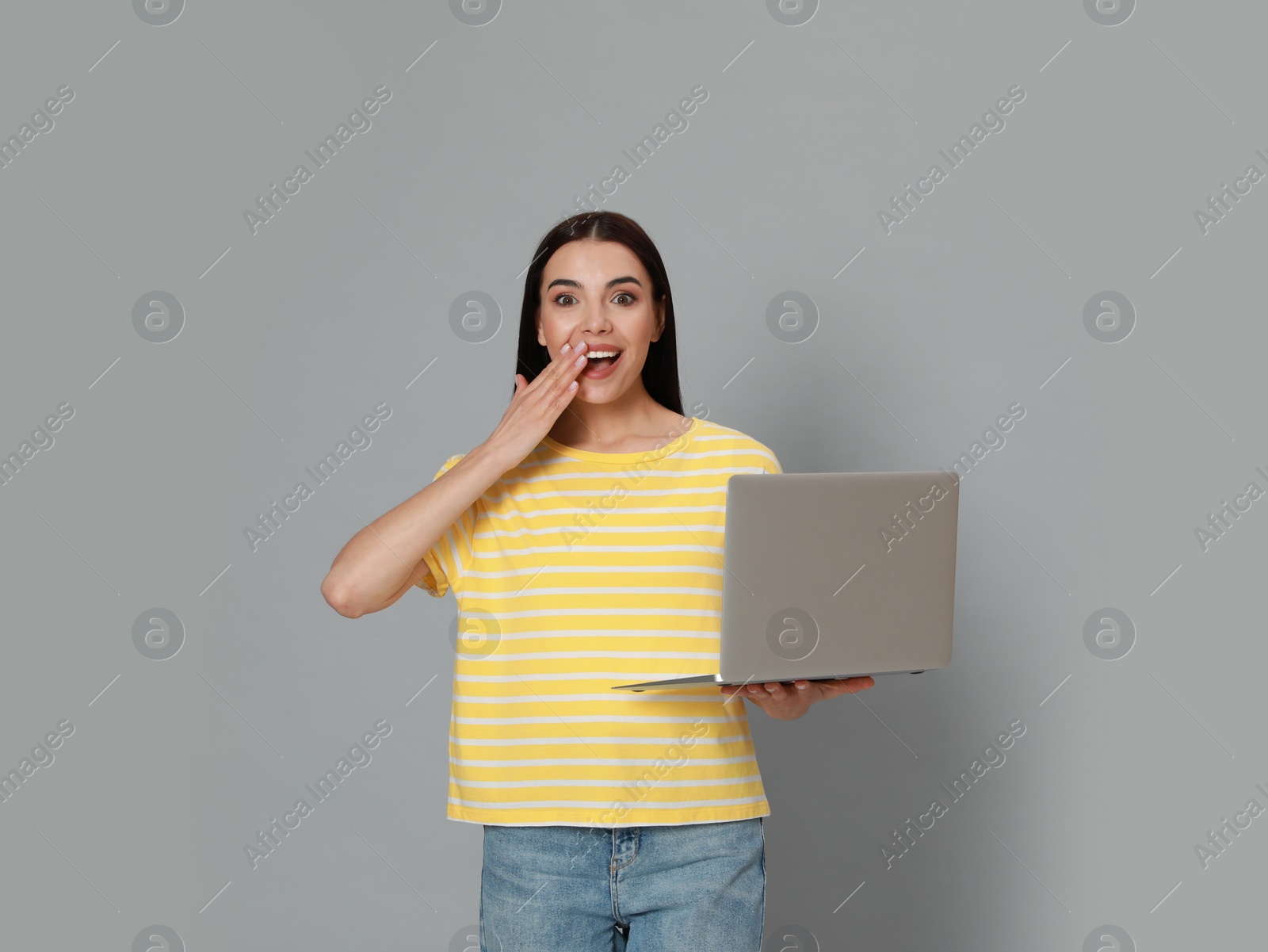 Photo of Emotional young woman with modern laptop on light grey background