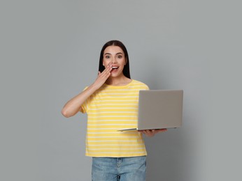 Emotional young woman with modern laptop on light grey background