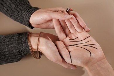 Photo of Chiromancer reading lines on woman's palm against color background, closeup