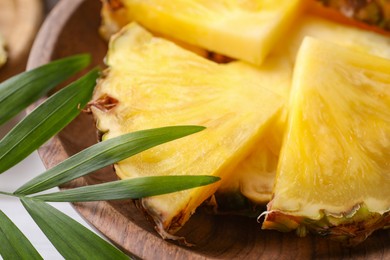 Photo of Pieces of tasty ripe pineapple in bowl and green leaves, closeup