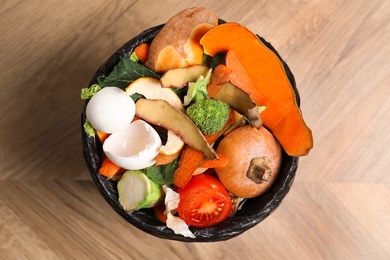 Photo of Trash bin with organic waste for composting on wooden background, top view
