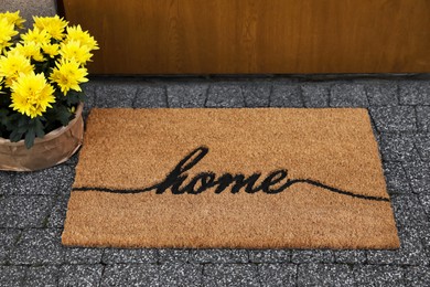 Doormat with word Home and flowers near entrance outdoors