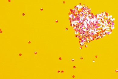 Photo of Heart made with shiny glitter on yellow background, flat lay