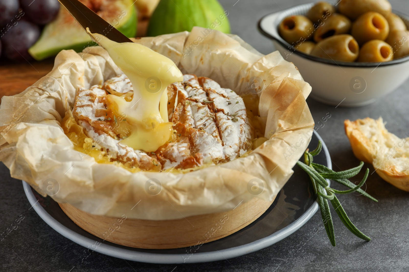 Photo of Taking tasty baked brie cheese with knife on grey table, closeup
