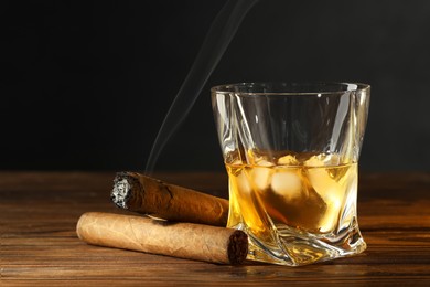 Photo of Glass of whiskey with ice cubes and cigars on wooden table