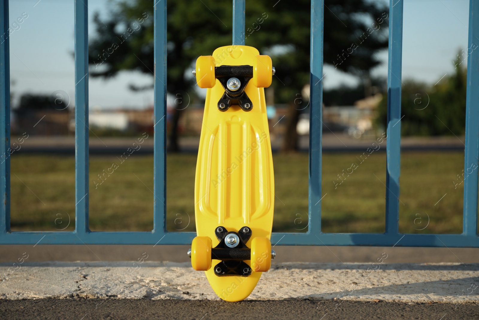 Photo of Modern yellow skateboard near fence outdoors on sunny day