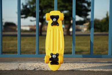 Modern yellow skateboard near fence outdoors on sunny day