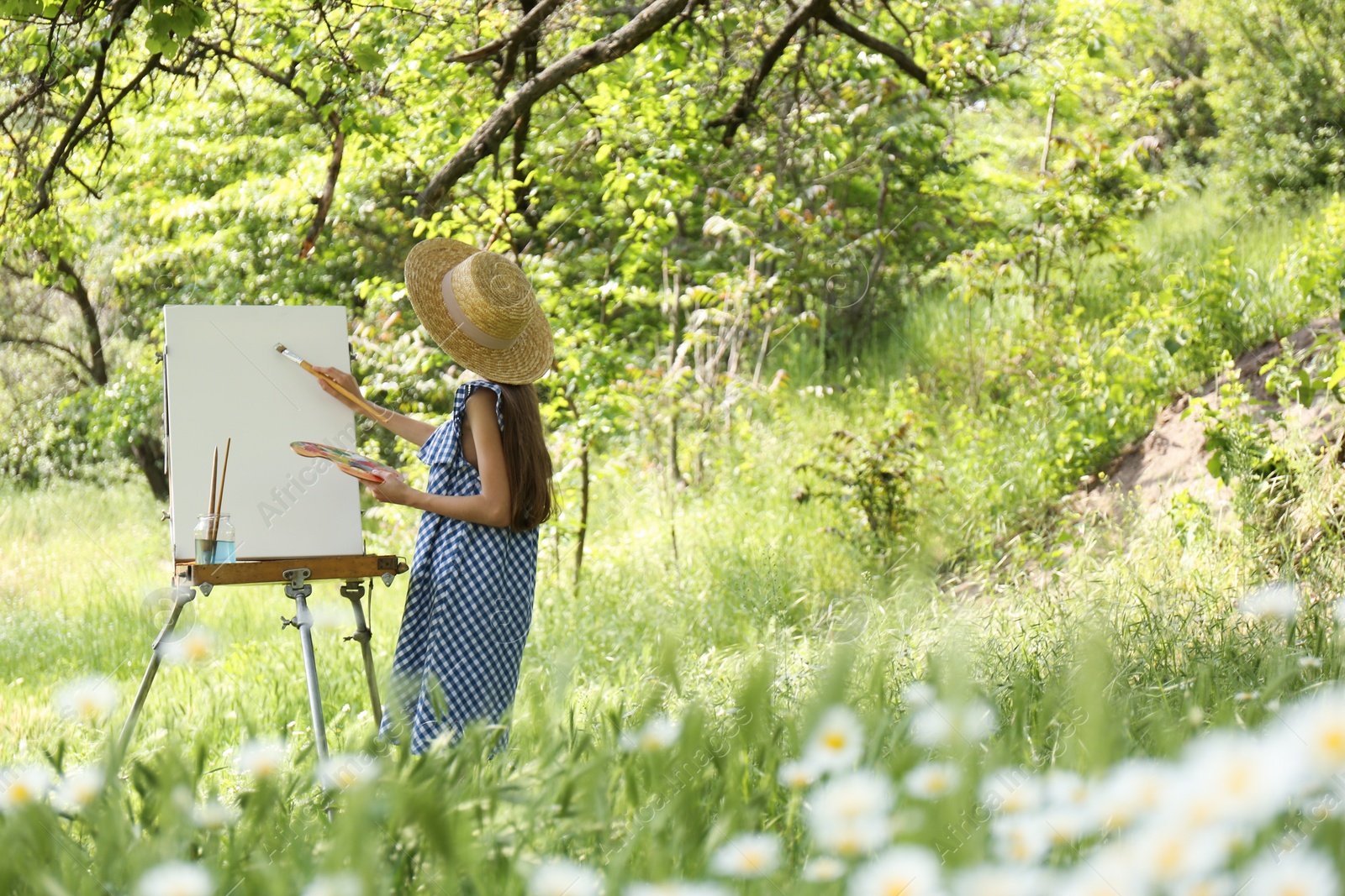 Photo of Little girl painting on easel in picturesque countryside