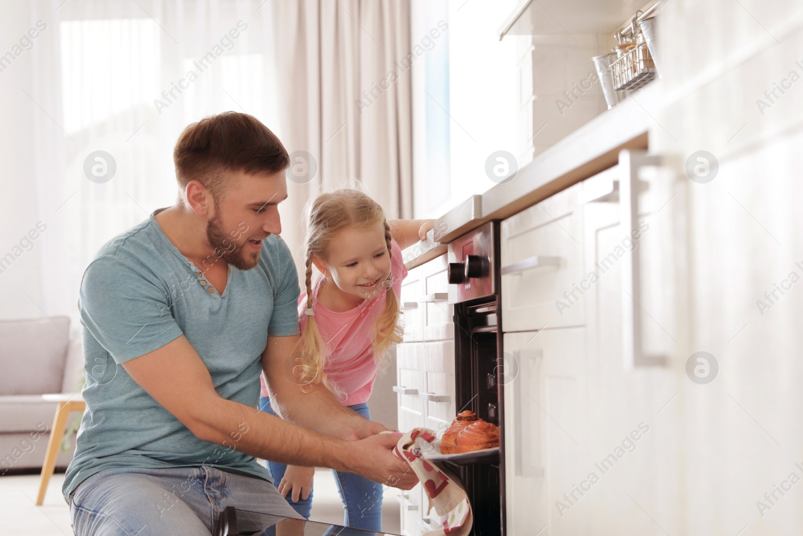 Photo of Father and daughter taking out buns from oven in kitchen