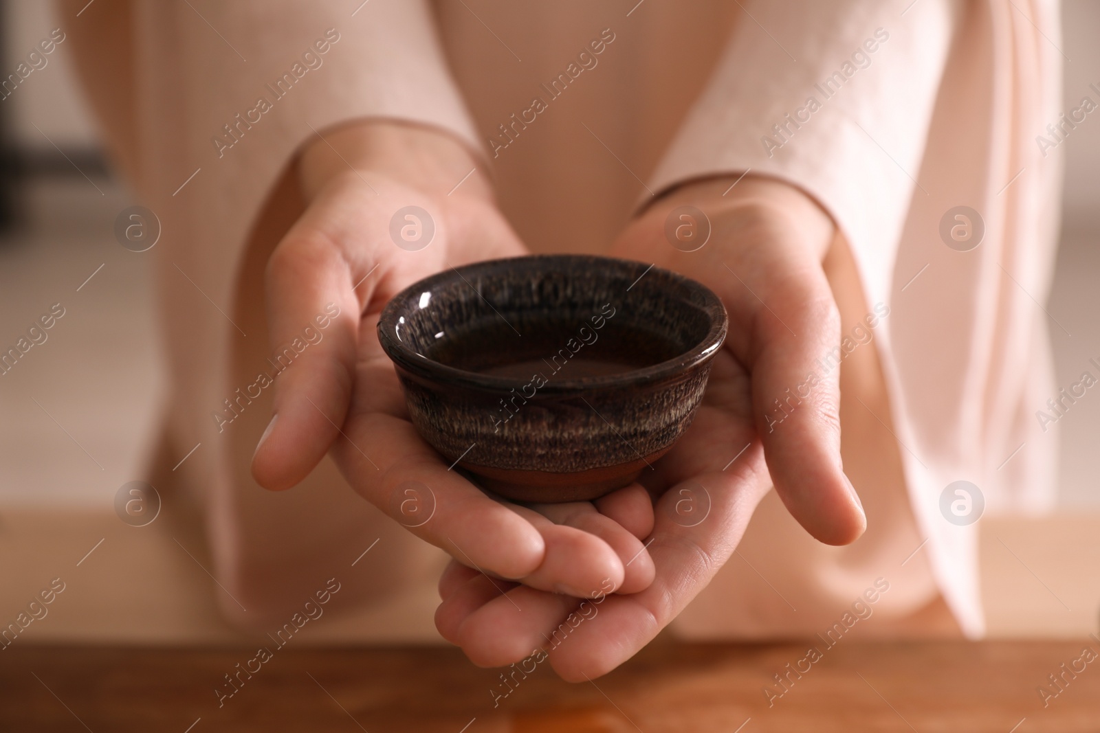 Photo of Master offering cup of freshly brewed tea during traditional ceremony at table, closeup