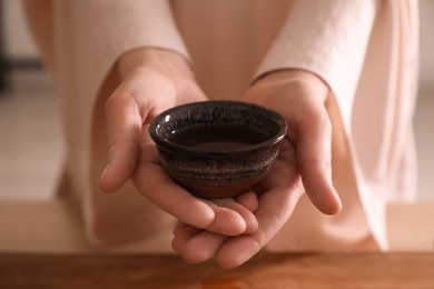 Photo of Master offering cup of freshly brewed tea during traditional ceremony at table, closeup