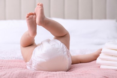 Photo of Little baby and stack of diapers on bed, closeup