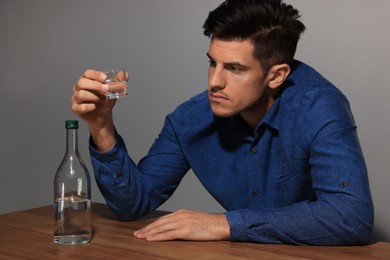 Photo of Addicted man with alcoholic drink at wooden table indoors