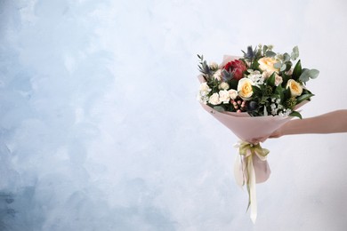 Photo of Woman with bouquet of beautiful roses on light blue background, closeup. Space for text