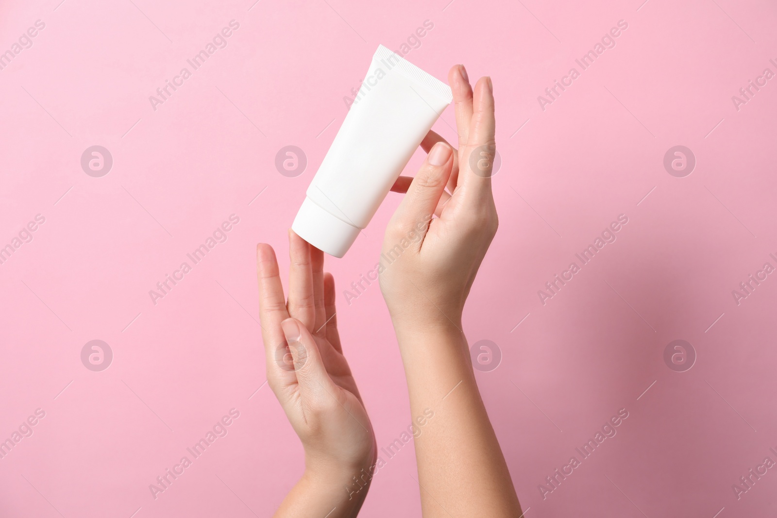 Photo of Woman with tube of hand cream on pink background, closeup