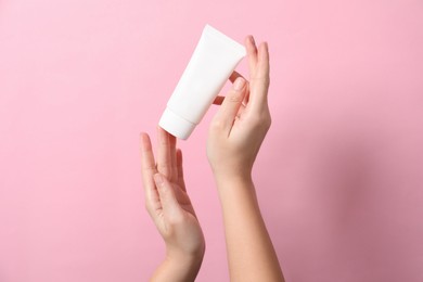 Photo of Woman with tube of hand cream on pink background, closeup