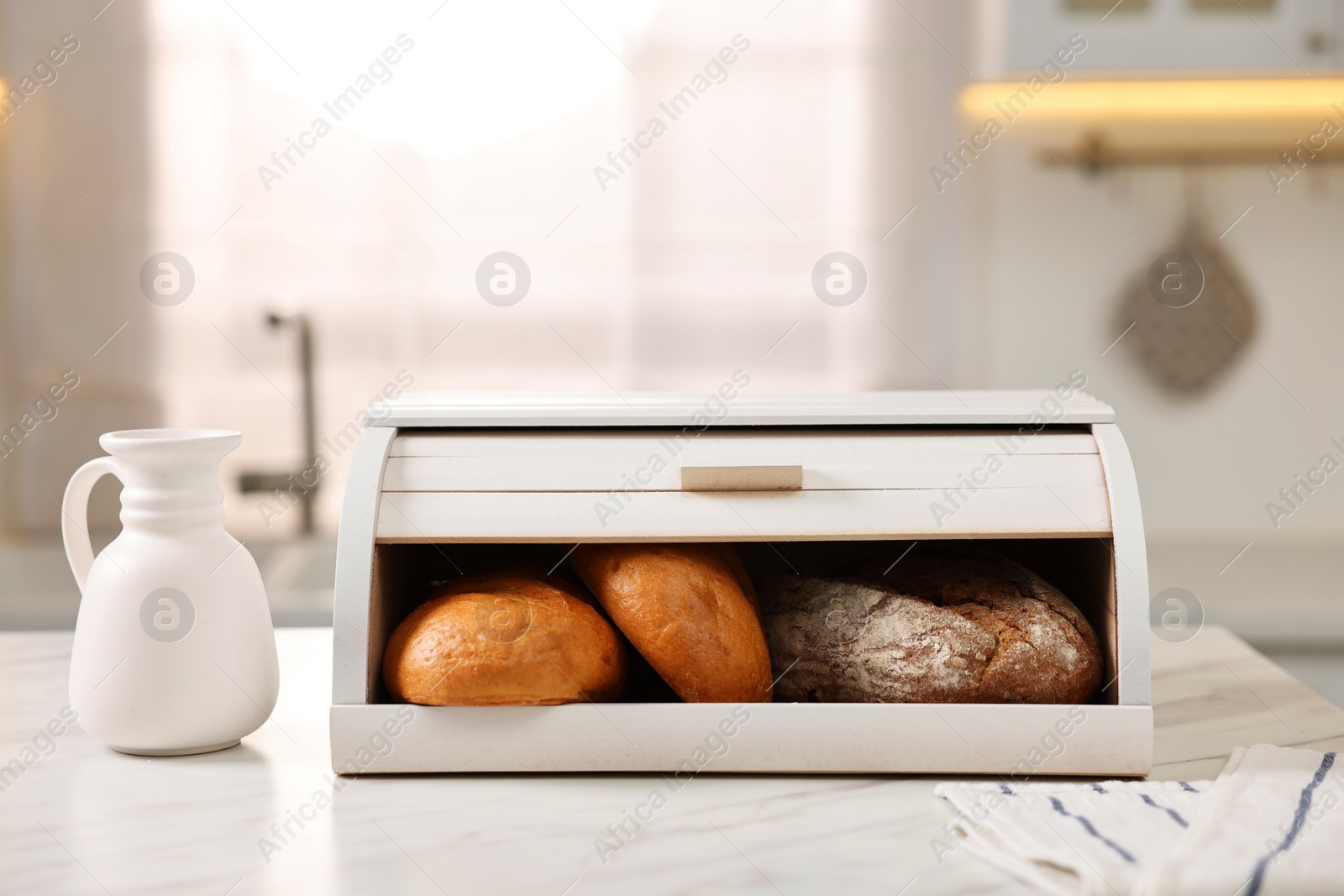 Photo of Wooden bread basket with freshly baked loaves on white marble table in kitchen