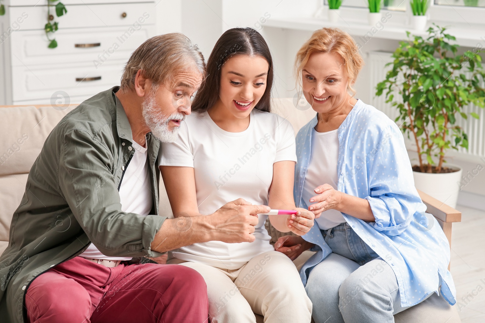 Photo of Happy woman showing her parents pregnancy test at home. Grandparents' reaction to future grandson