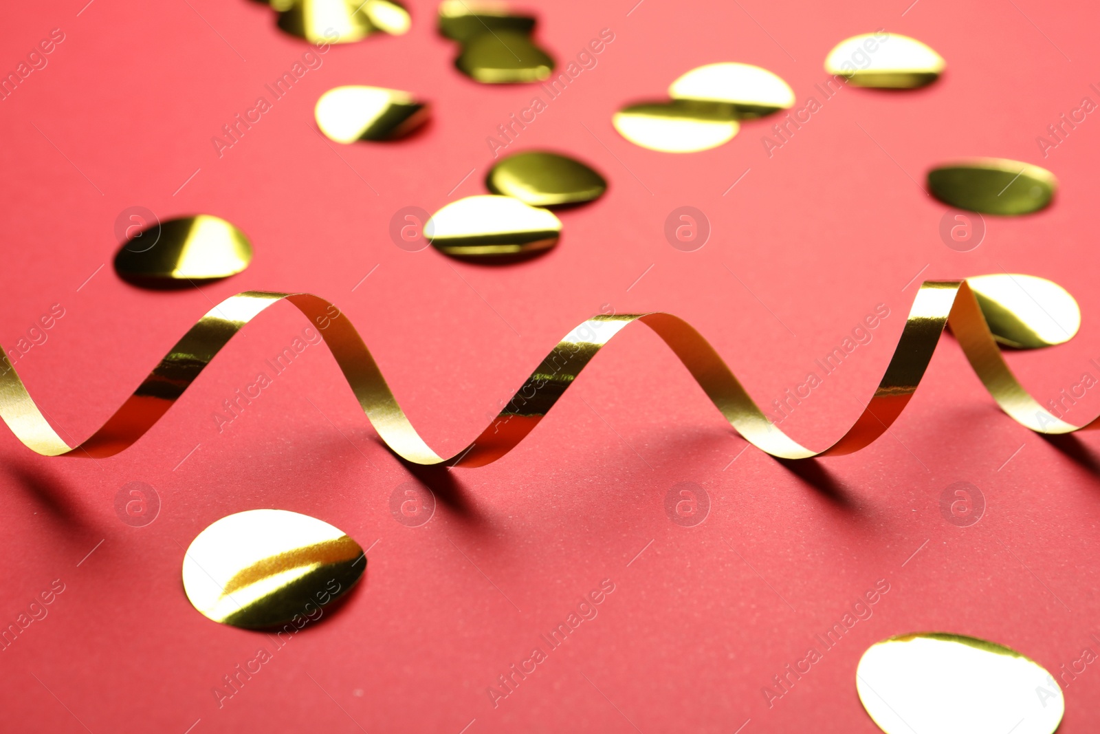 Photo of Shiny golden serpentine streamer and confetti on red background, closeup