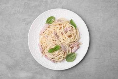 Photo of Plate of tasty pasta Carbonara with basil leaves on grey table, top view