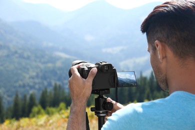 Photo of Man taking photo of nature with modern camera on stand outdoors