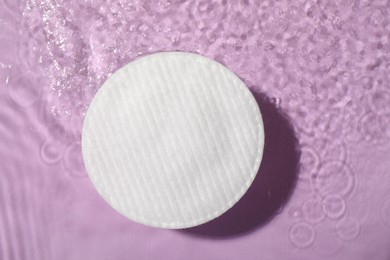 Photo of Cotton pad and micellar water on violet background, top view