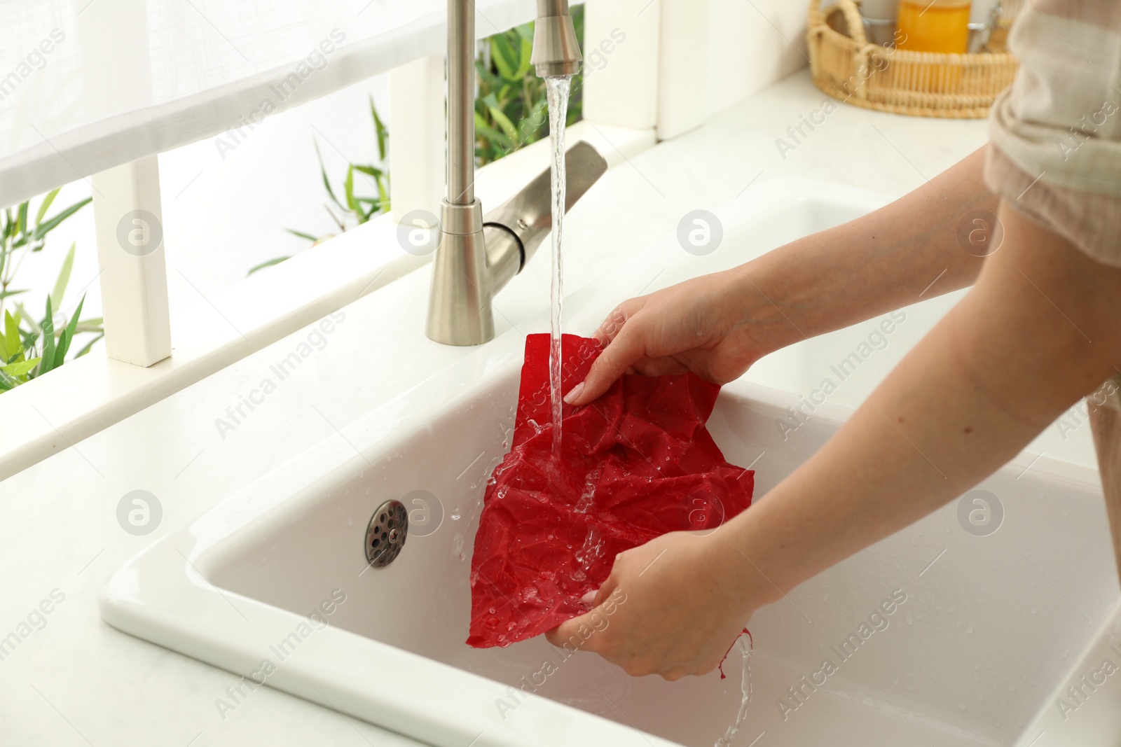 Photo of Woman washing beeswax food wrap under tap water in kitchen sink, closeup