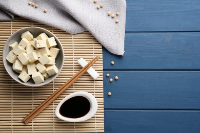 Photo of Cut tofu and soy sauce served on blue wooden table, flat lay. Space for text