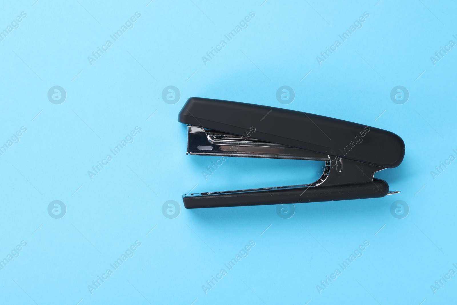 Photo of Black stapler on light blue background, top view. Space for text