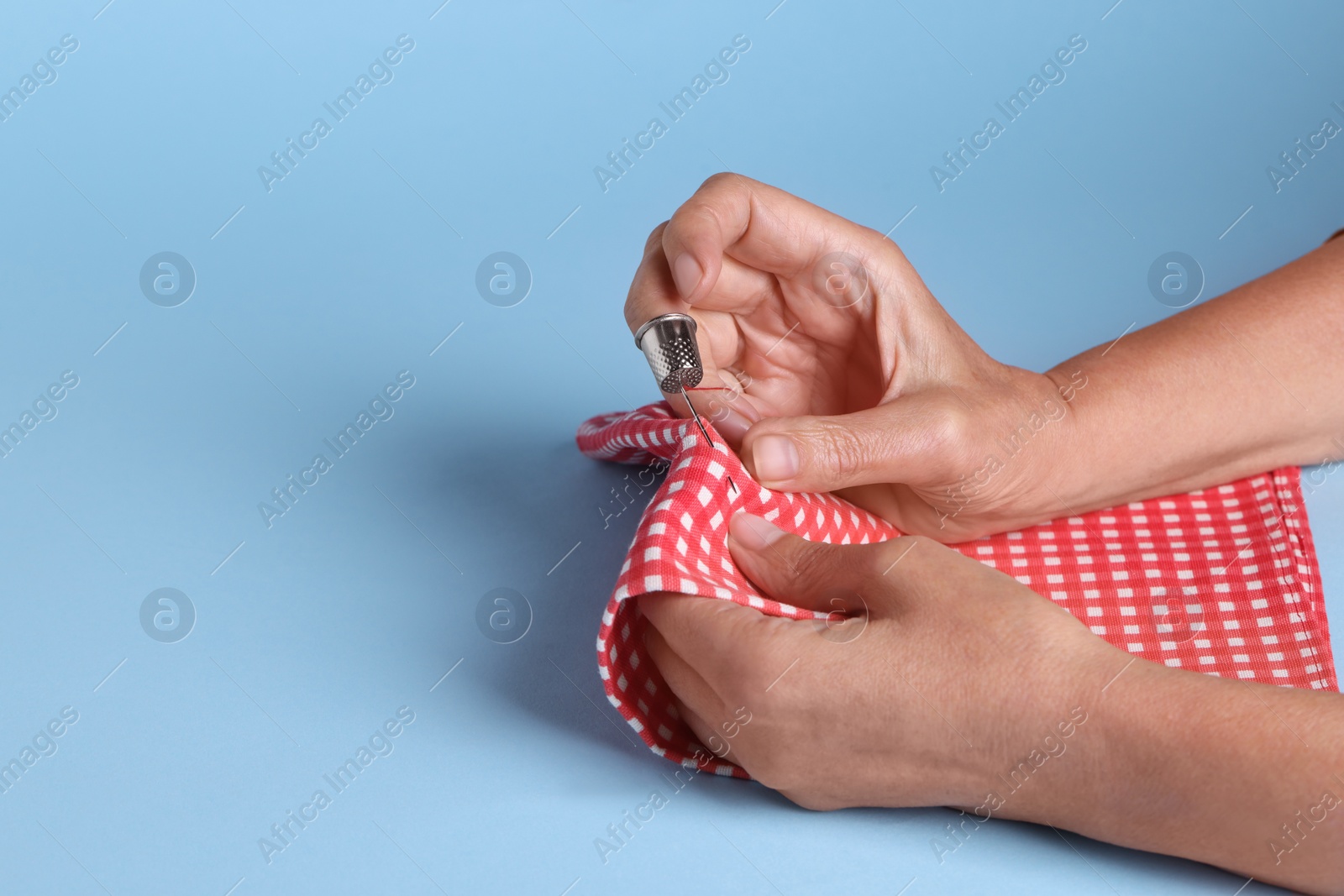 Photo of Woman sewing with thimble and needle on light blue background, closeup. Space for text