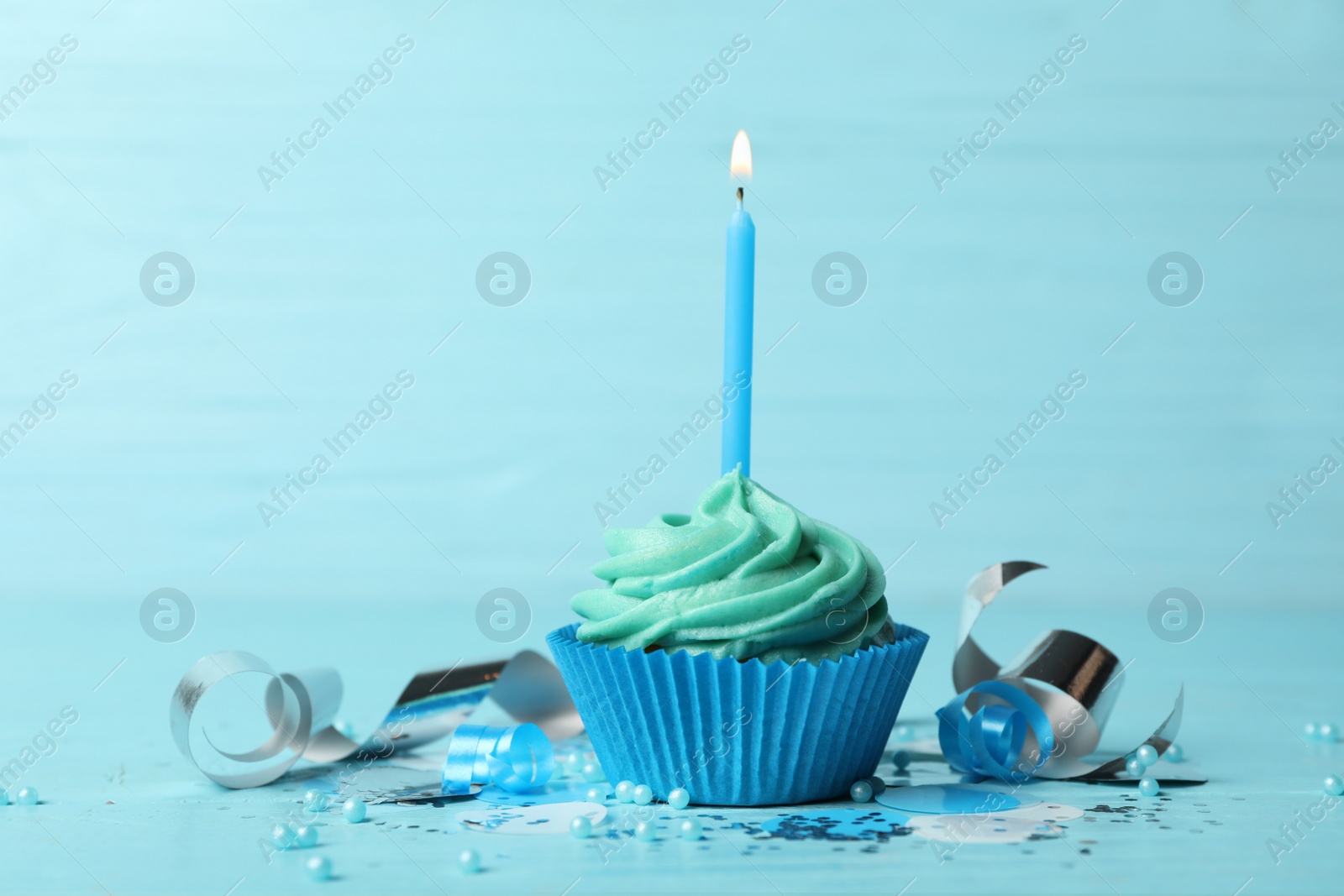 Photo of Delicious birthday cupcake with cream and burning candle on blue wooden background