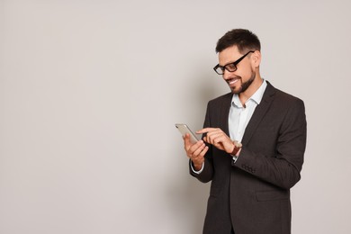 Photo of Handsome man in suit looking at smartphone on light grey background. Space for text