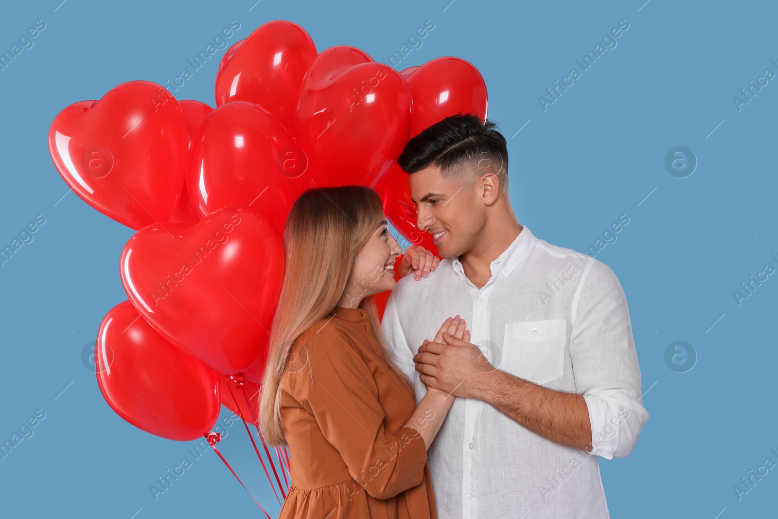 Photo of Lovely couple with heart shaped balloons on light blue background. Valentine's day celebration