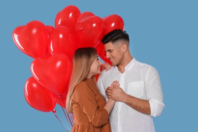 Lovely couple with heart shaped balloons on light blue background. Valentine's day celebration