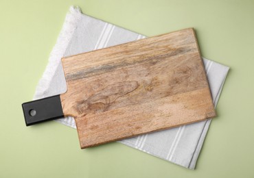 Wooden board and napkin on light olive background, top view