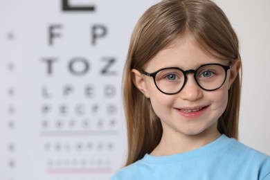 Photo of Little girl with glasses against vision test chart